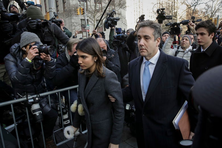 Cohen walks past a barricade amid a crowd of photographers while holding his daughter's arm.